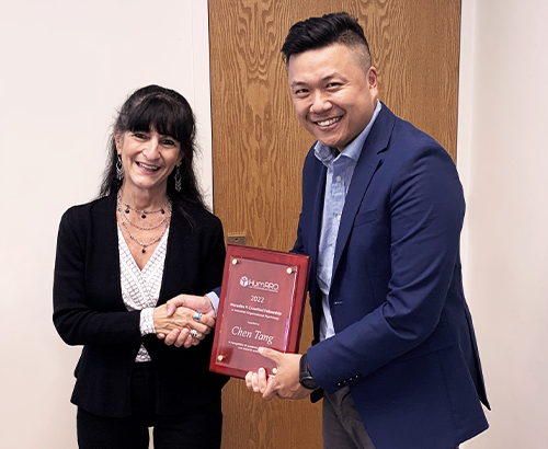 Suzanne Tsacoumis and Chen Tang shaking hands, Chen Tang holding and displaying the award Suzanne Tsacoumis and Chen Tang shaking hands, Chen Tang holding and displaying the award